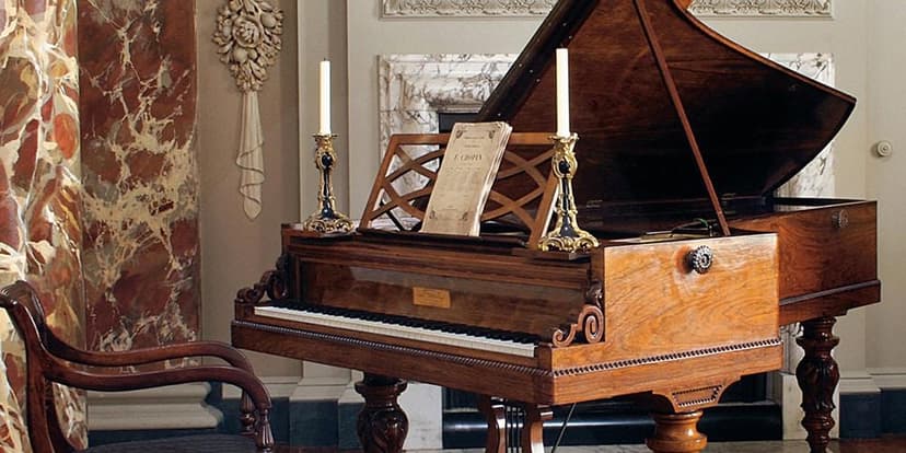 Старинный рояль Pleyel эпохи Шопена, с деревянным корпусом и изящными ножками, стоящий в комнате с картинами.
